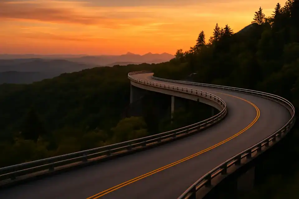 Winding mountain road at sunset with vibrant orange sky, scenic highway, elevated curves, forested hills, scenic drive, summer sunset, elevated roadway, mountain landscape, travel destination, picturesque sunset, nature scenery.